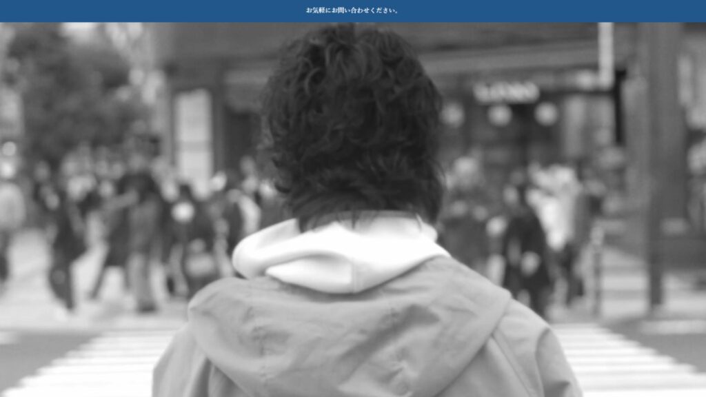 街の交差点で立ち止まる人物を後ろから撮影したモノクロ写真。映像で人の物語や感情を表現するビデオグラファーの作品イメージ。