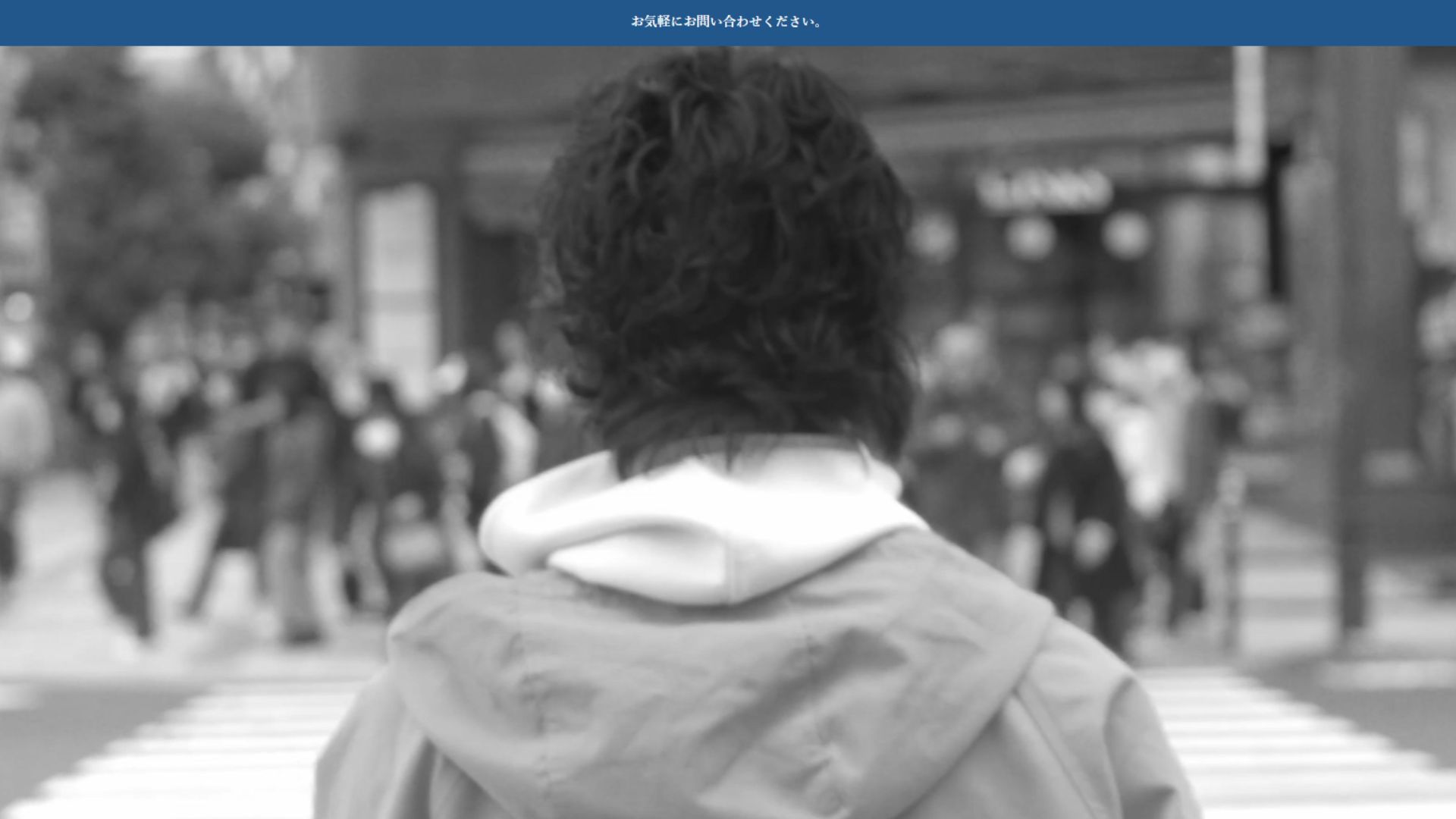 街の交差点で立ち止まる人物を後ろから撮影したモノクロ写真。映像で人の物語や感情を表現するビデオグラファーの作品イメージ。